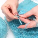Woman knitting with blue yarn.