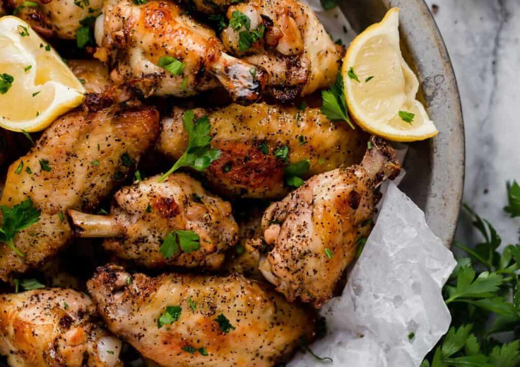 Chicken wings in a bowl with lemon and parsley.