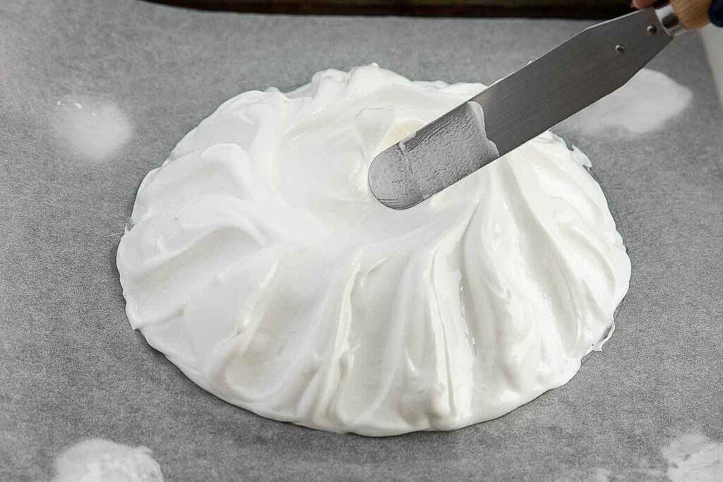 A person is using a knife to shape whipped egg whites for a pavlova.