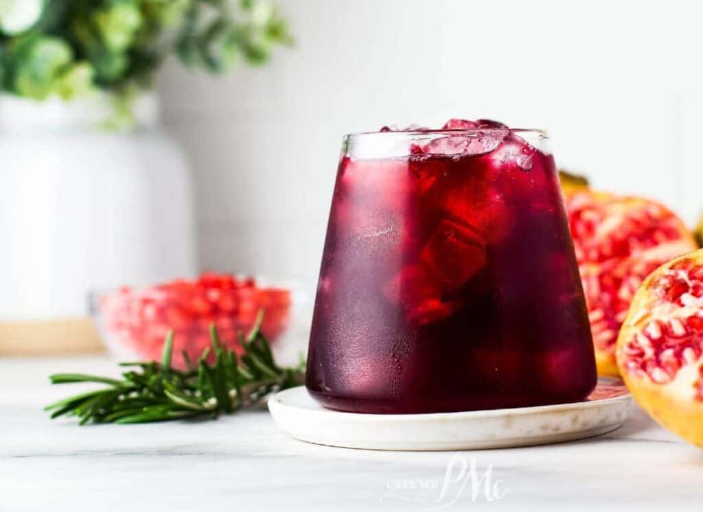 A glass of pomegranate juice with rosemary and pomegranate seeds.