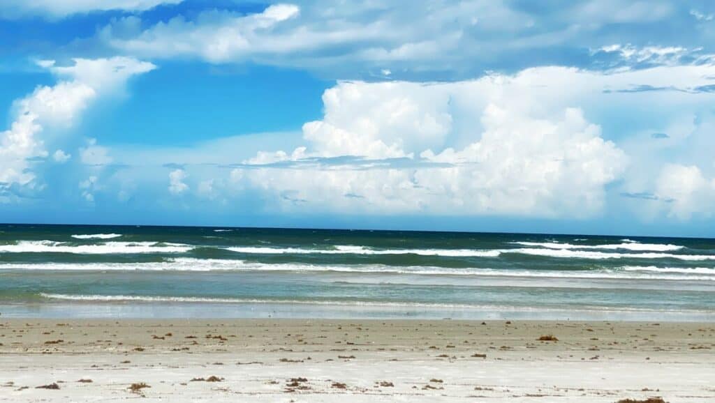 A man is standing on a beach with clouds in the sky, enjoying the breathtaking view of New Smyrna Beach.