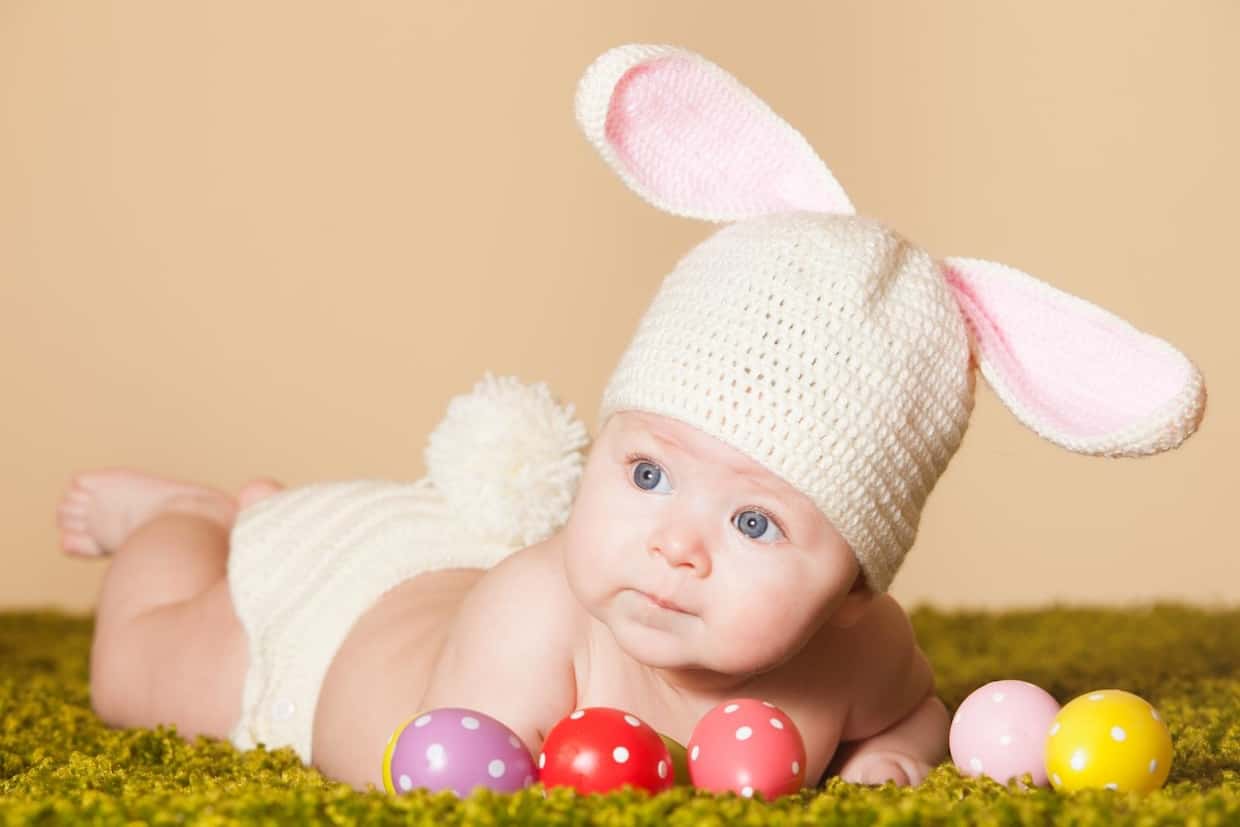 A newborn baby wearing a knitted bunny hat surrounded by easter eggs.