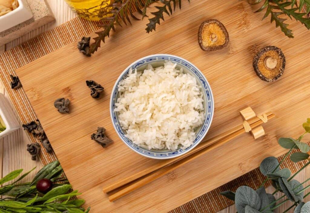 A bowl of rice and chopsticks on a wooden cutting board.