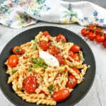 A bowl of pasta with cherry tomato sauce, cherry tomatoes, and garlic.