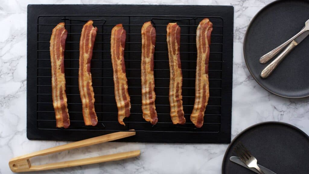 Bacon on a cooling rack next to serving tongs and serving plates.