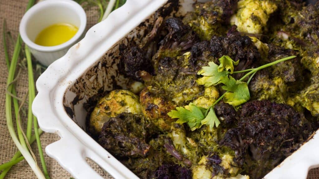 Cozy casserole featuring roasted cauliflower with pesto and parsley in a baking dish.
