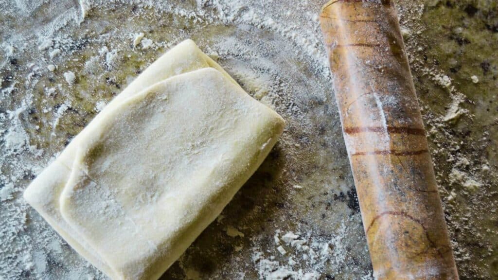 A piece of rough puff pastry dough and a rolling pin on a table.