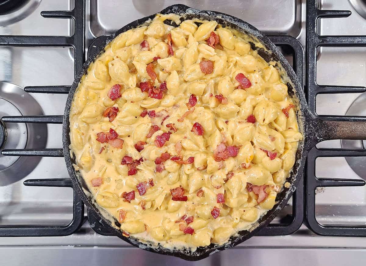 A skillet filled with smoked mac and cheese and bacon on a stove top.