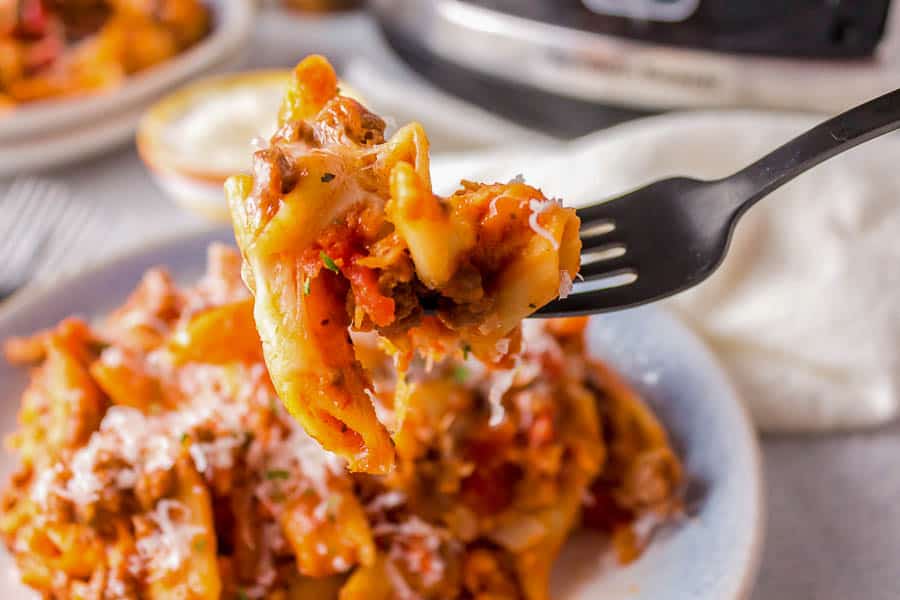 A fork is being used to take a bite of cheesy penne out of an instant pot.