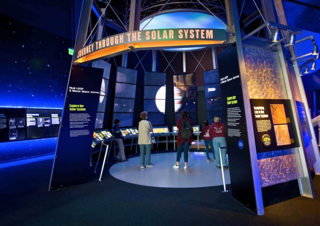 A group of people are looking at an exhibit about the solar system.
