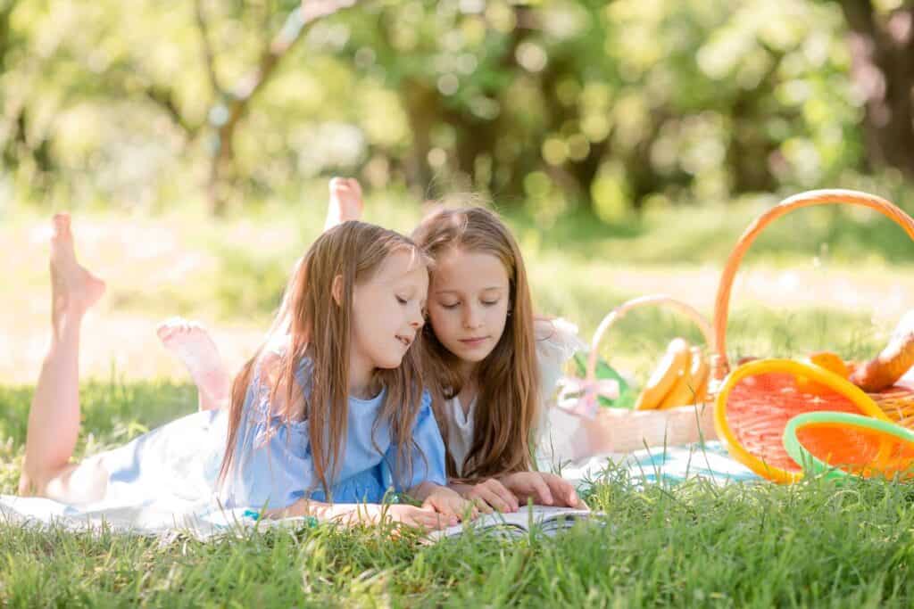 Two little girls laying on the grass reading a book.
