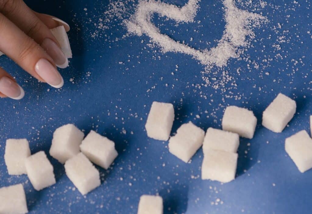 A woman's hand is touching sugar cubes, on a blue background.