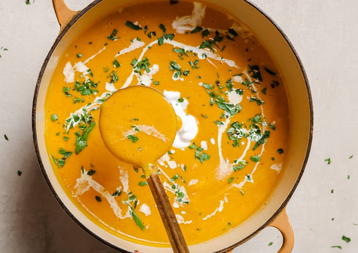 A pot of sweet potato and red pepper soup with sour cream and parsley.