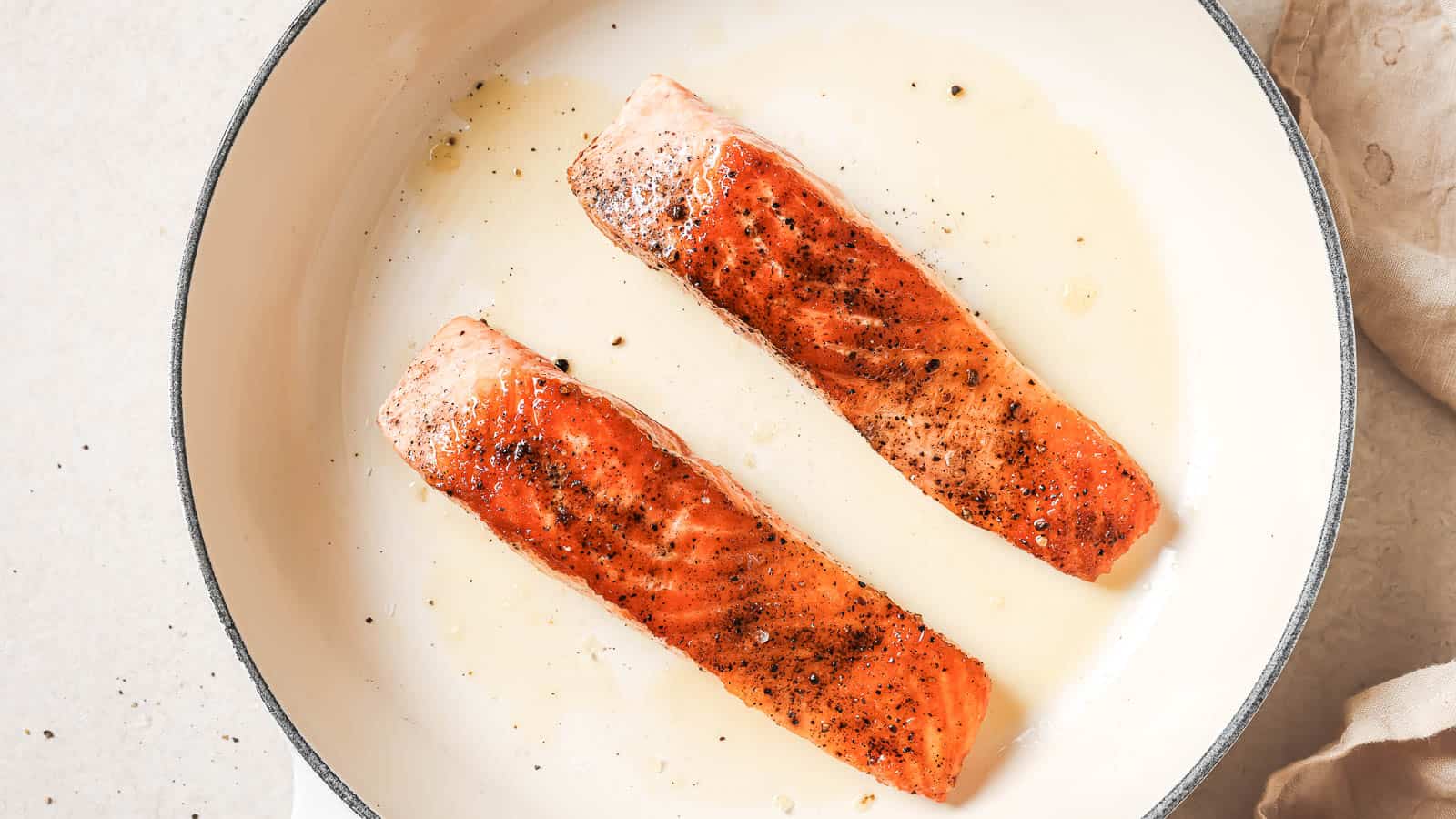 Two salmon fillets in a white skillet.
