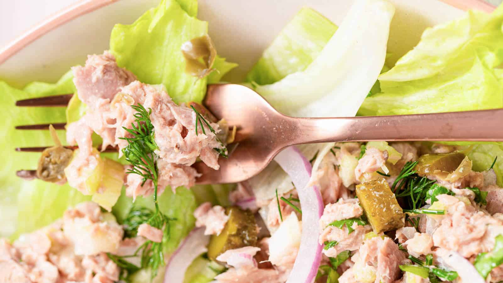 Healthy Tuna salad without mayo sits on a bed of iceberg lettuce surrounded by two forks, dill, and a green linen.