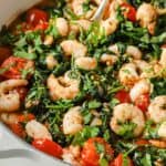 A pan full of shrimp, tomatoes and spinach.