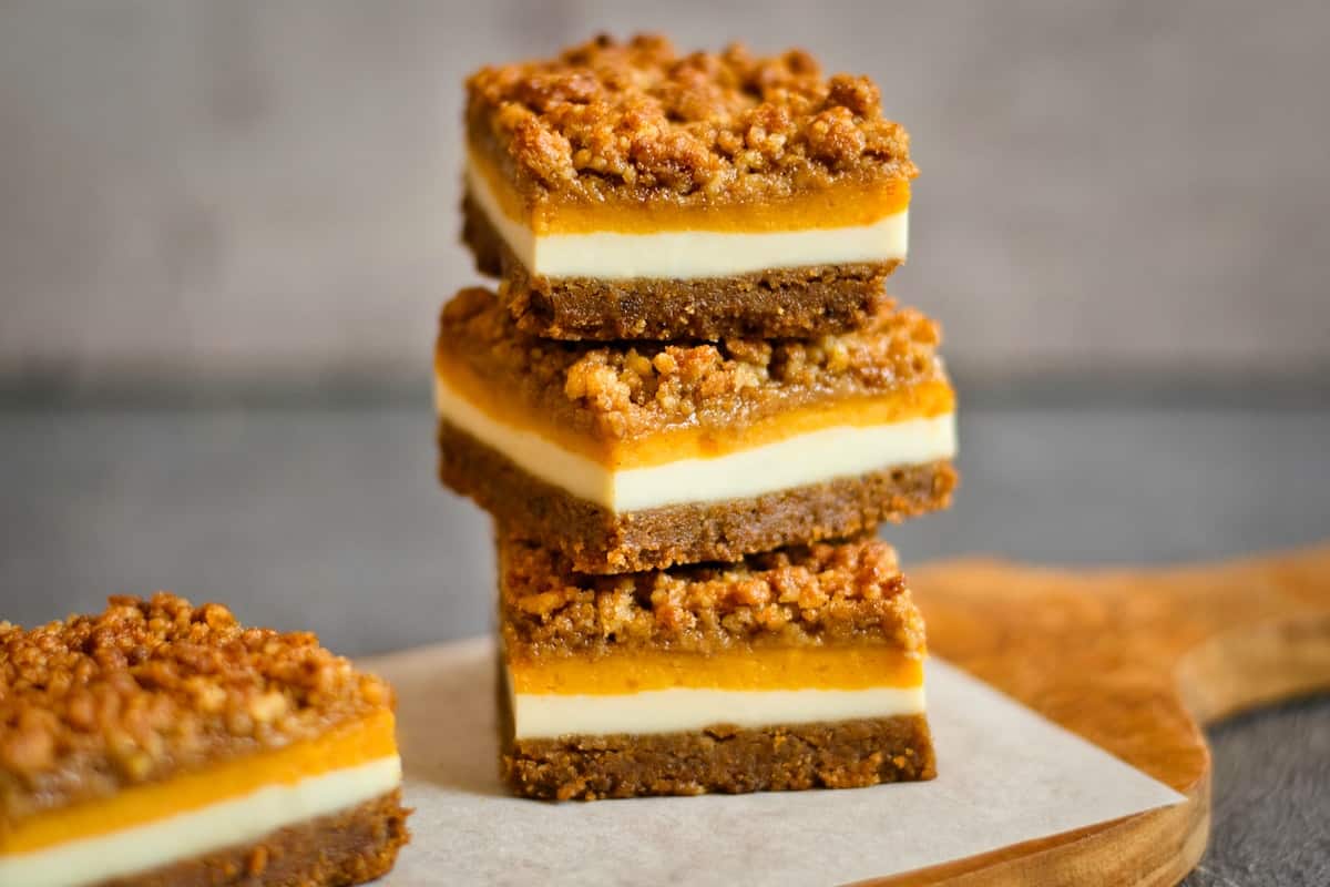 Stack of three pumpkin cheesecake bars on a flat surface.