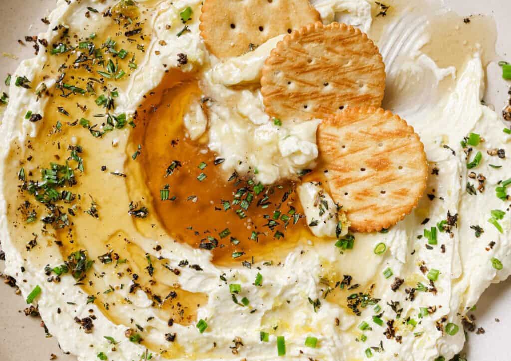 A bowl of whipped feta with honey with crackers and herbs.