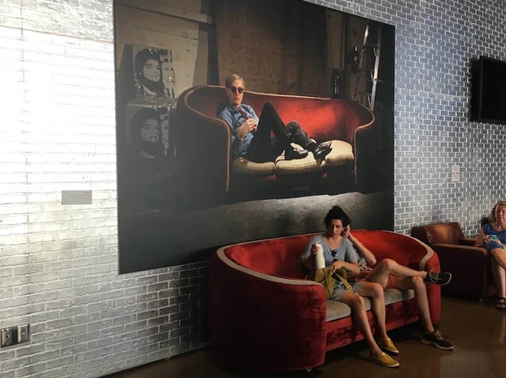 Two people sitting on a red couch in front of a large painting.
