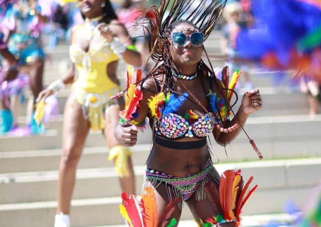 A woman dressed in colorful feathers is dancing in the street.