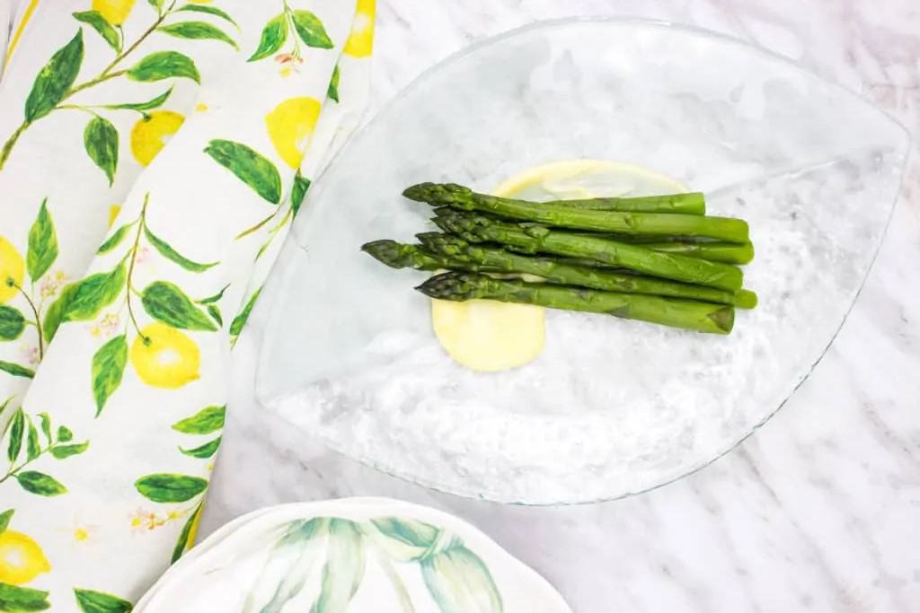 A plate of asparagus with lemon sauce on it.