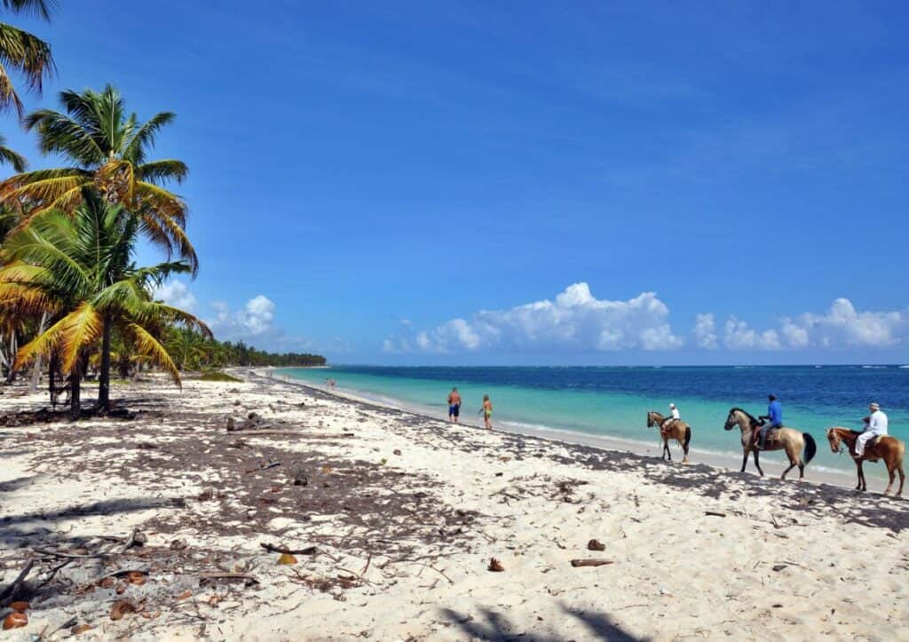 A group of people riding horses on a sandy beach.