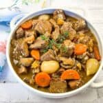 Beef bourguignon in a white bowl with thyme.