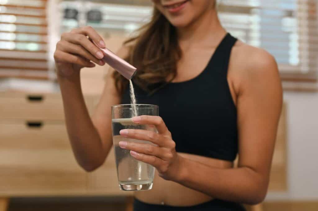 A woman pouring water into a glass while exploring the benefits of collagen powder.