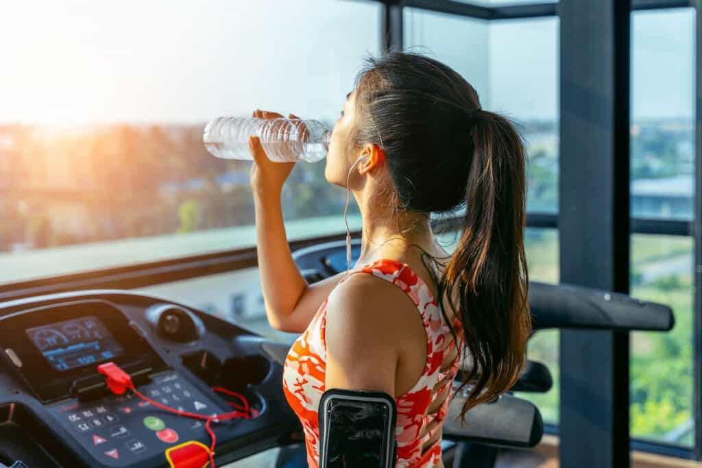 A woman staying hydrated while exercising on a treadmill and using the best water enhancers.