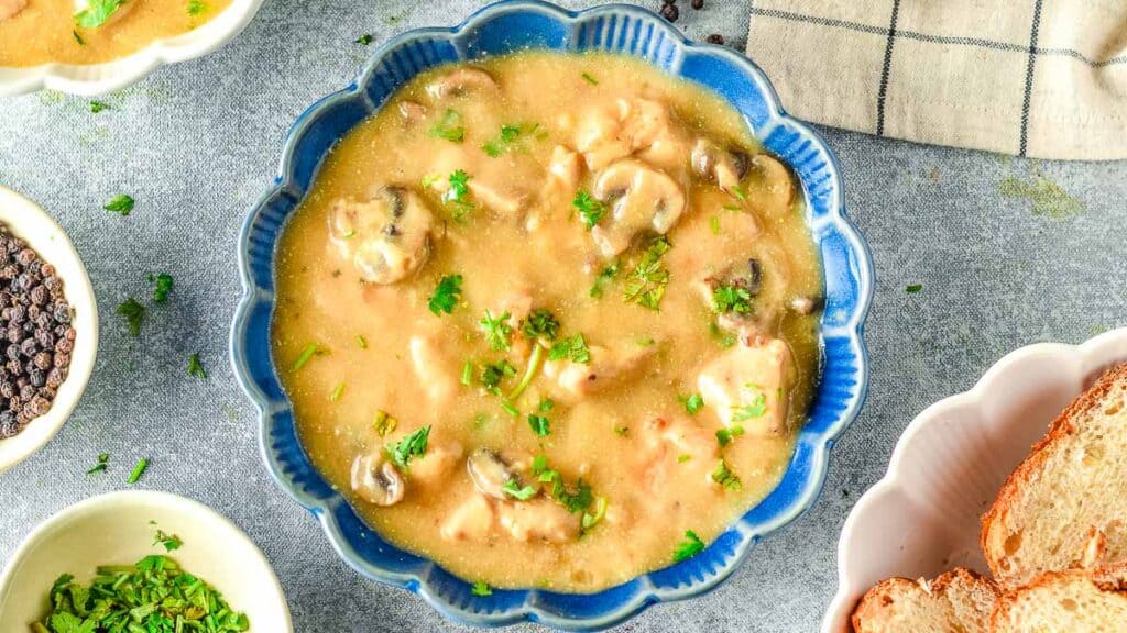 A bowl of chicken and mushroom soup with bread and parsley.