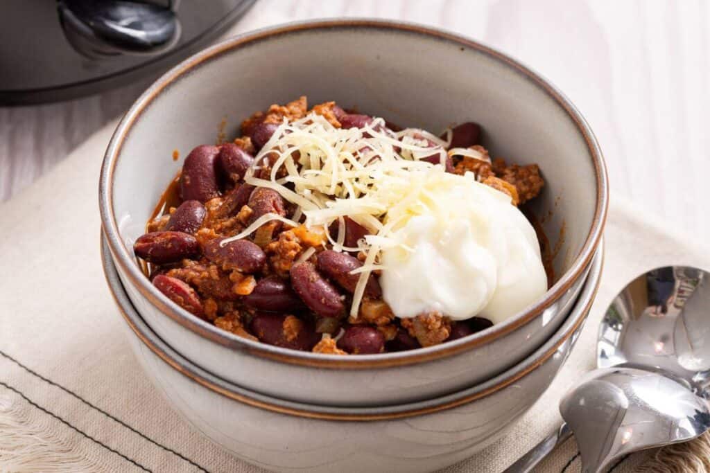 A bowl of chili with cheese and sour cream.