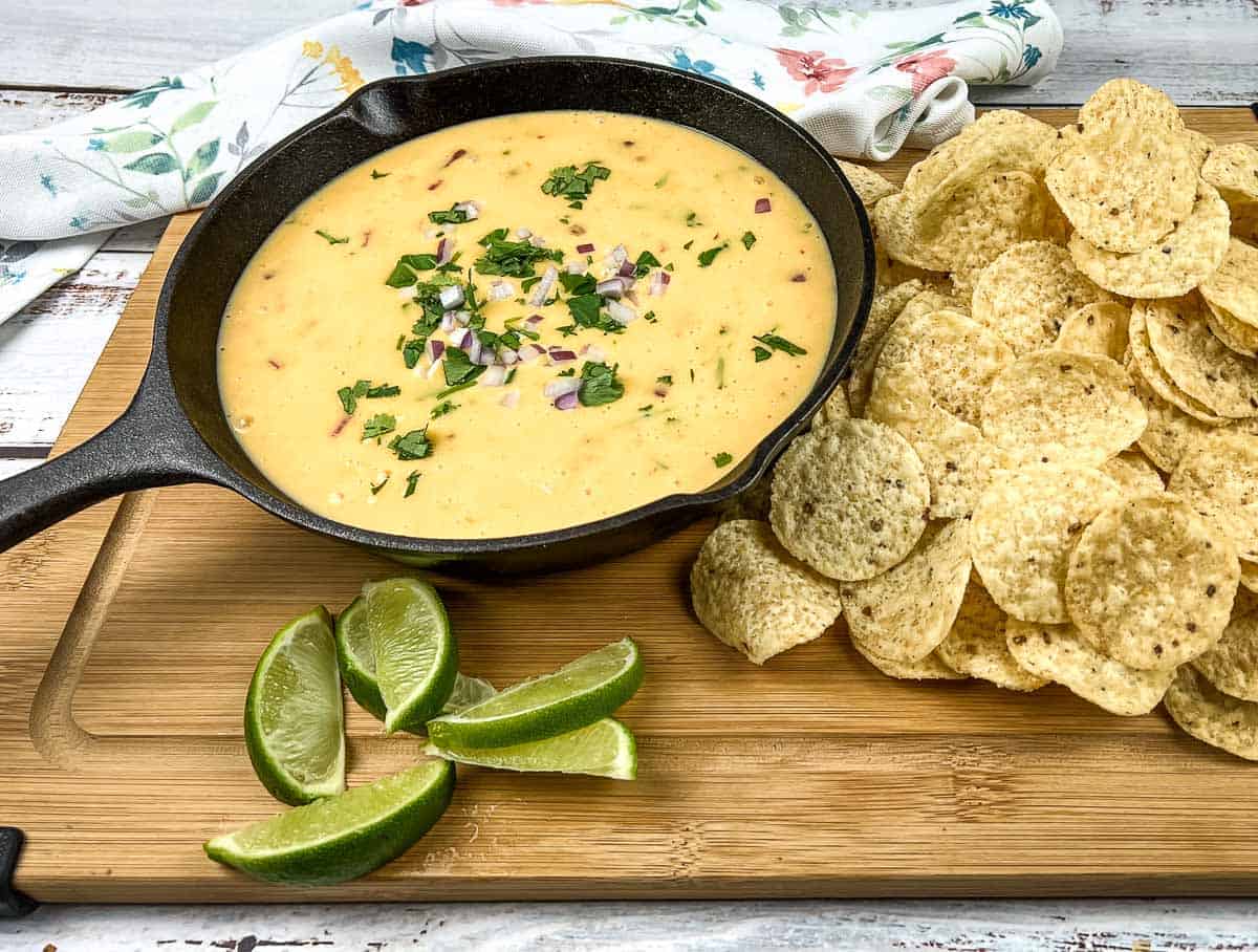 Velveeta queso in a skillet with tortilla chips and lime wedges.