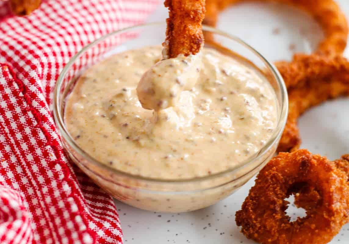 An onion ring being dipped into Spicy Dipping Sauce.
