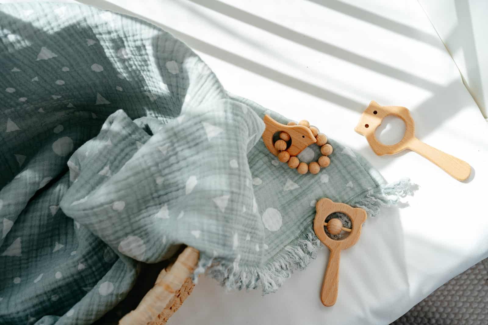 Eco-friendly swaddle blanket and wooden teether on a bed.