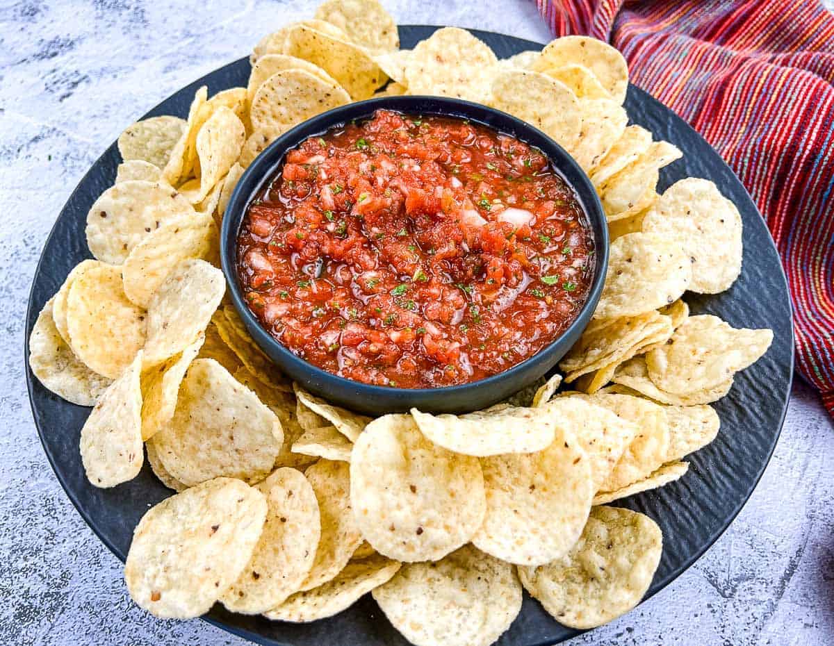 Homemade salsa on a black plate with tortilla chips.