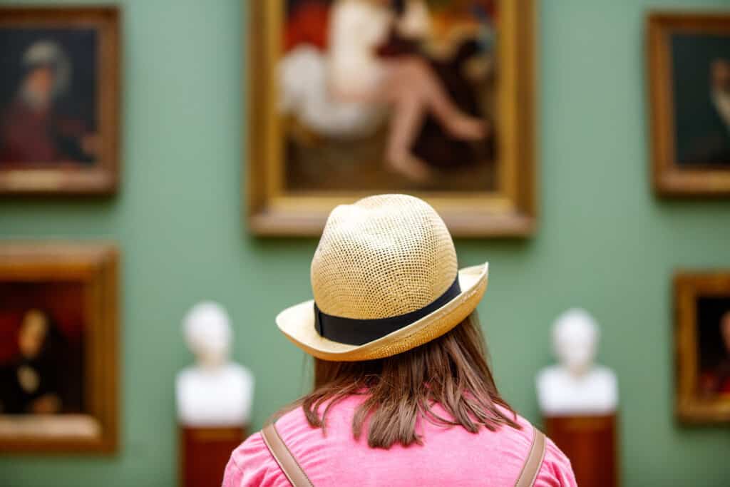 A woman in a hat looking at paintings in a museum.
