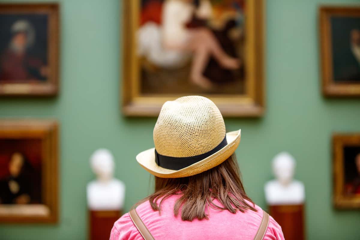 Girl in a hat looking at museum paintings.