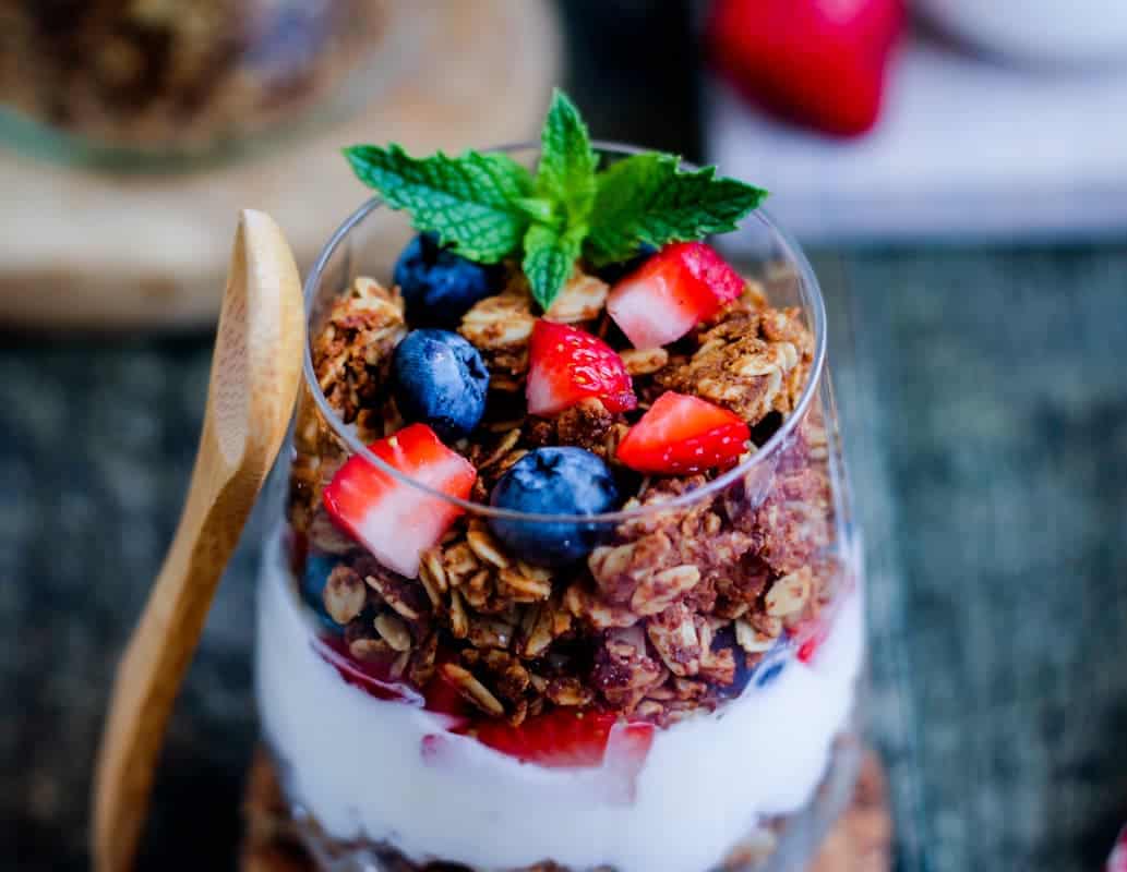 A parfait in a glass layered with yogurt and gluten free granola.