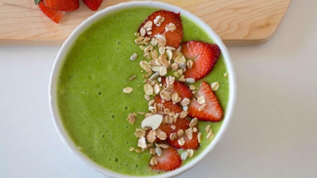 A bowl of green smoothie with strawberries and granola.