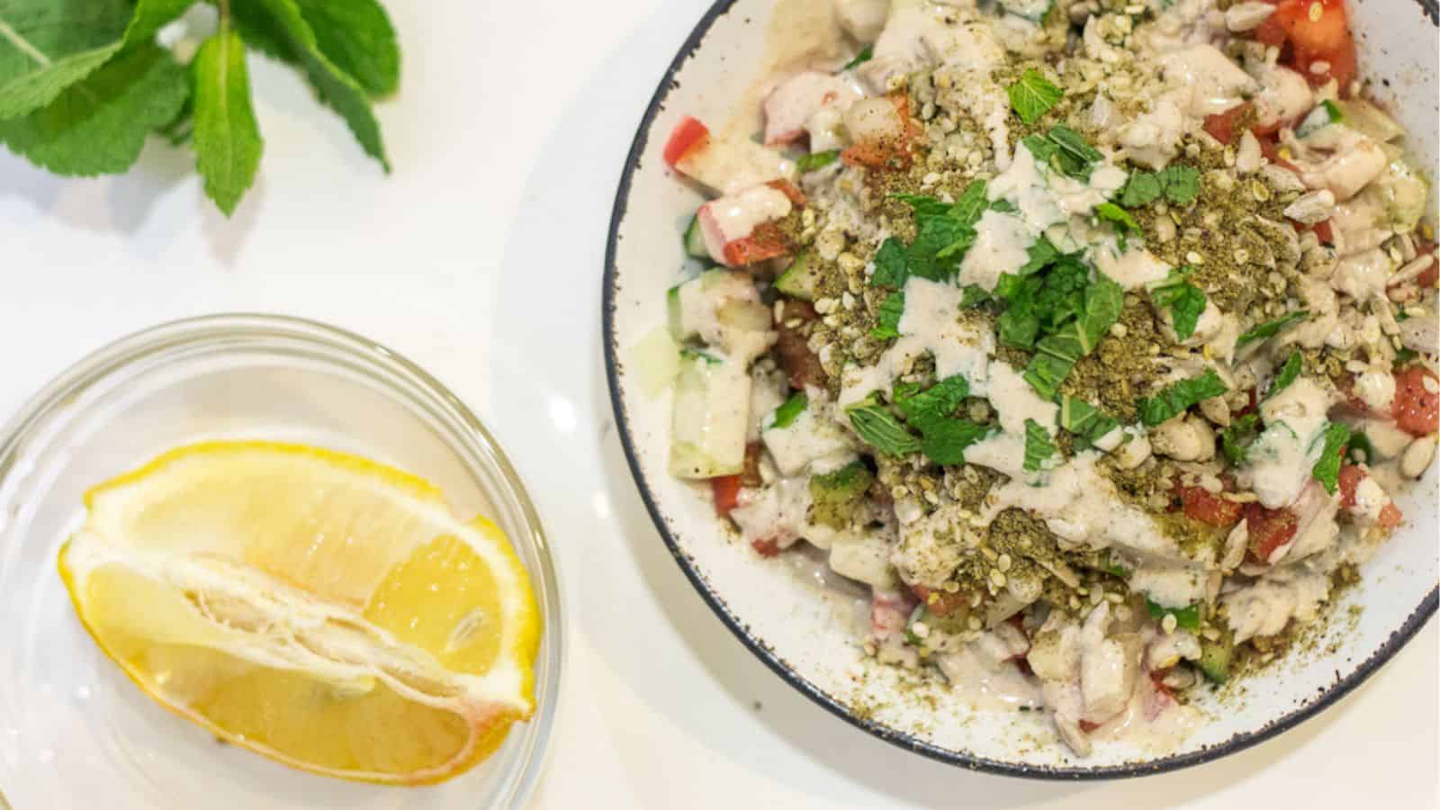 A bowl of salad with a slice of lemon next to it.