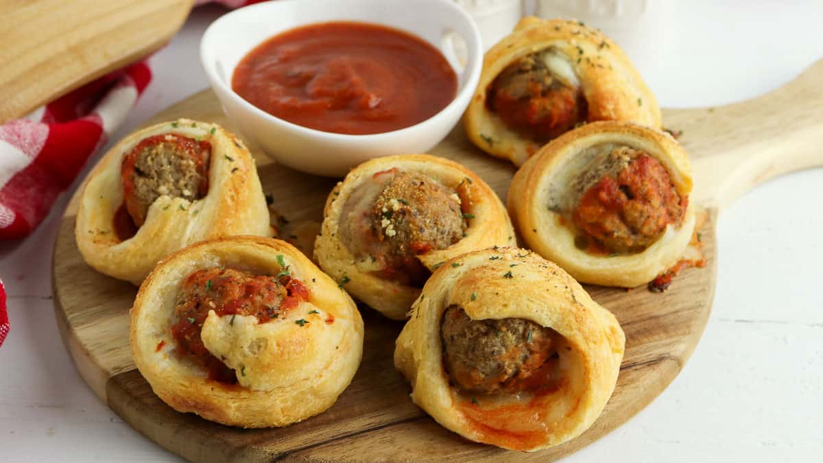 Meatballs wrapped in dough on a wooden cutting board.