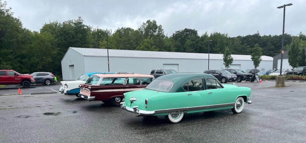 Three classic cars parked in a parking lot while visiting a museum.