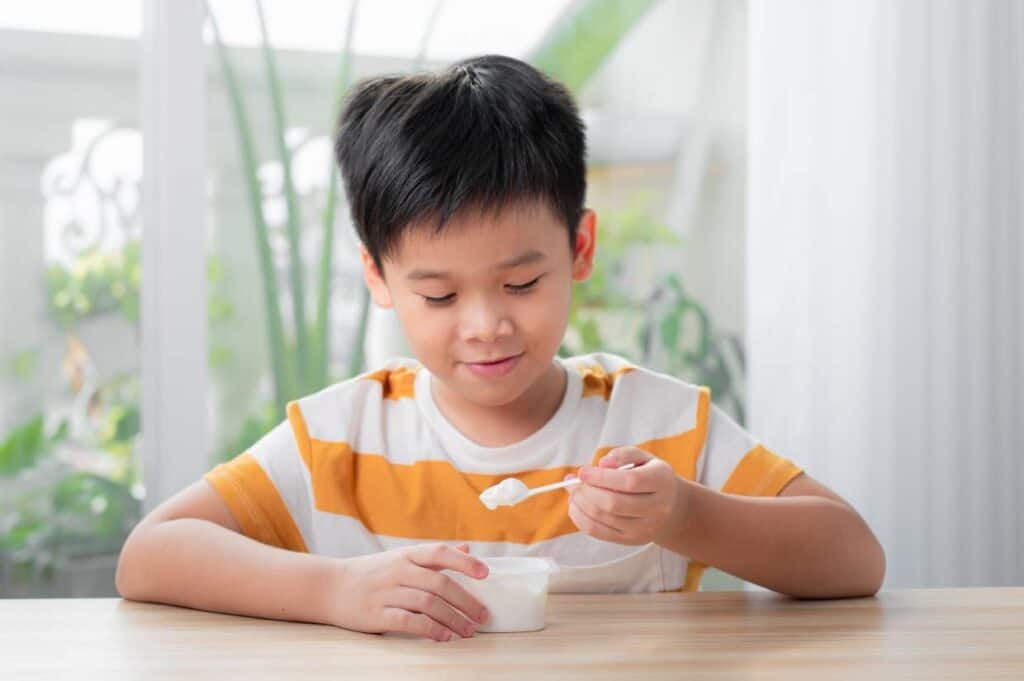 A young asian boy eating a spoon of yogurt.