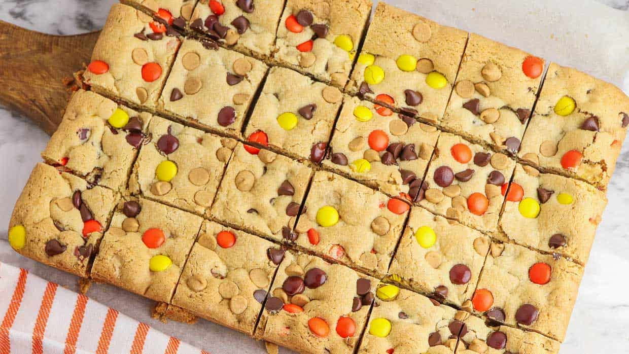A square of Reeses pieces cookie bars on a cutting board.
