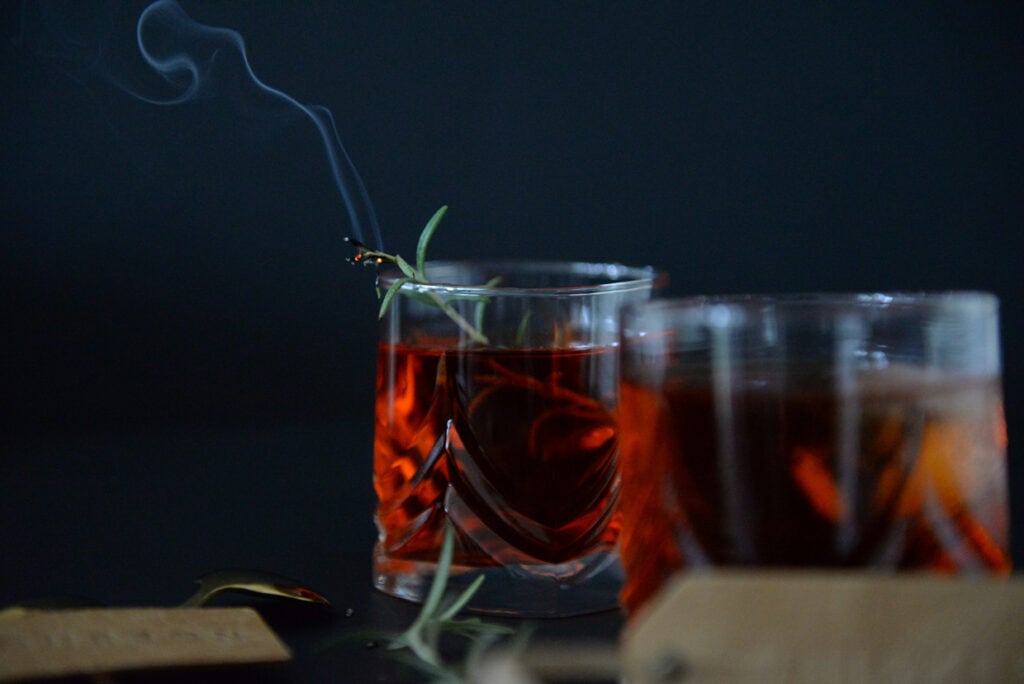 A glass of red wine with a sprig of rosemary.