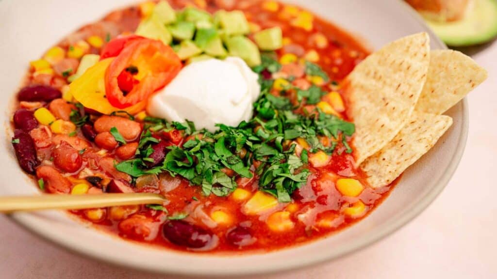 A bowl of mexican bean and corn soup with sour cream and avocado.