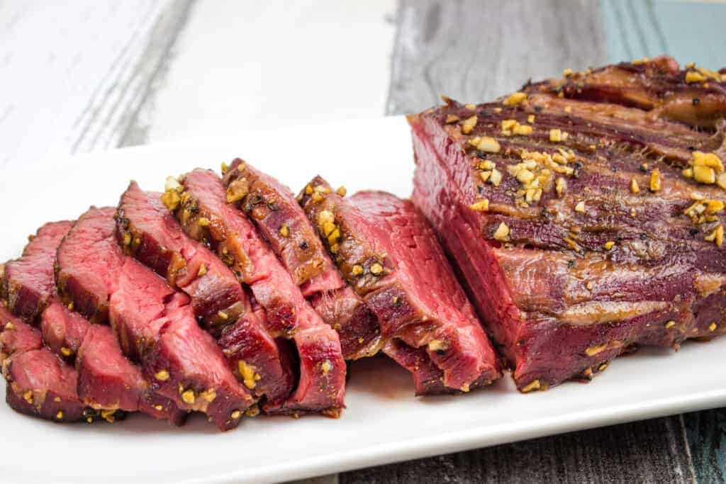 A sliced smoked beef tenderloin on a white plate.