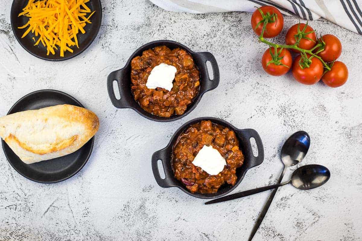 Two bowls of smoked brisket chili, tomatoes, and bread.
