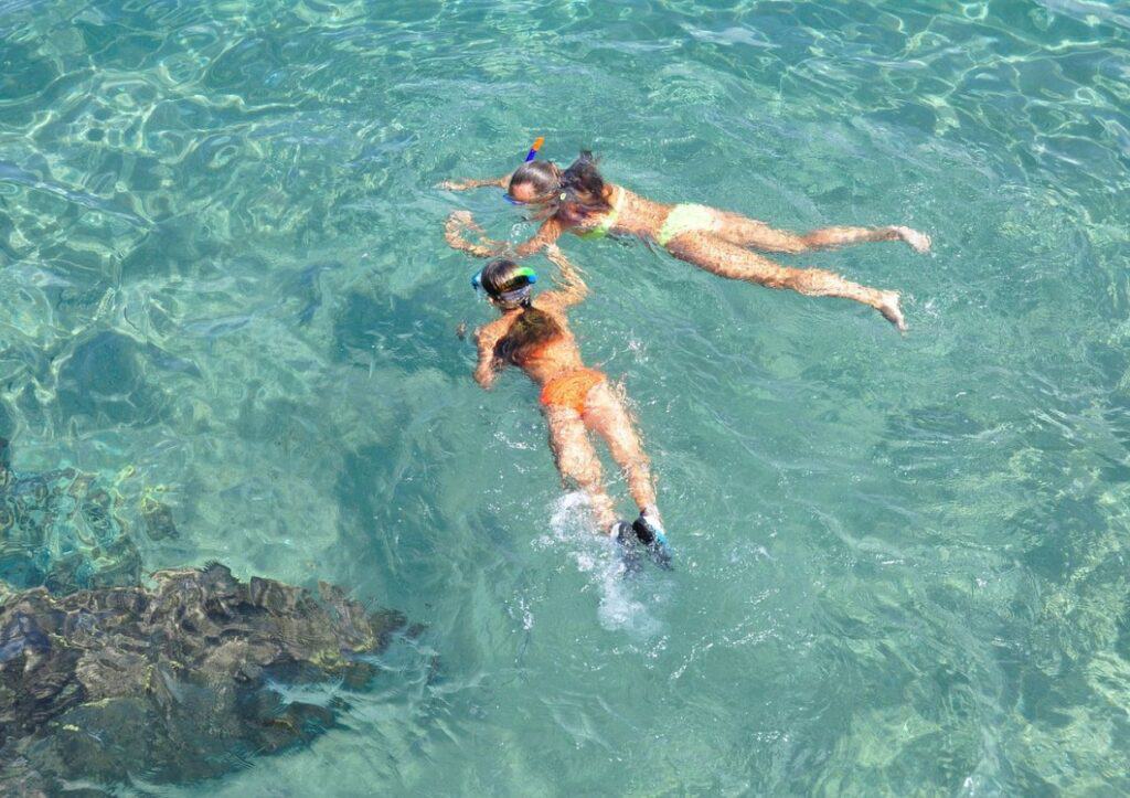 Two women snorkling in the clear blue water.