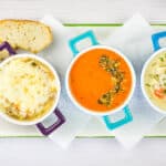 Three bowls of soup with bread on a plate.